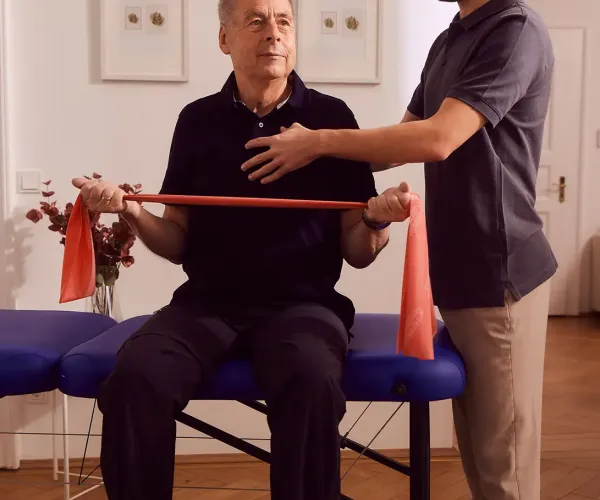 Mann trainiert mit Theraband, unterstützt von Physiotherapeut in Praxis.