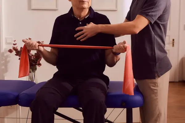 Mann trainiert mit Theraband, unterstützt von Physiotherapeut in Praxis.