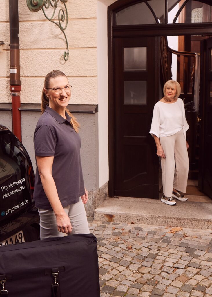Mobile Physiotherapeutin kommt mit Auto bei ihrer Patientin zu Hause an und trägt die mobile Therapiebank zum Hauseingang.