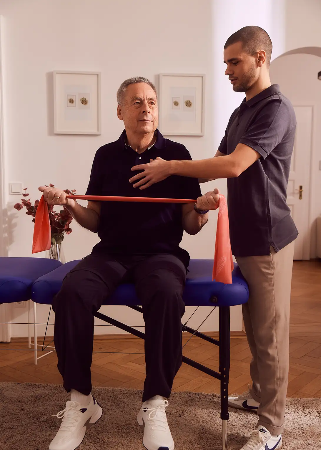 Mann trainiert mit Theraband, unterstützt von Physiotherapeut in Praxis.