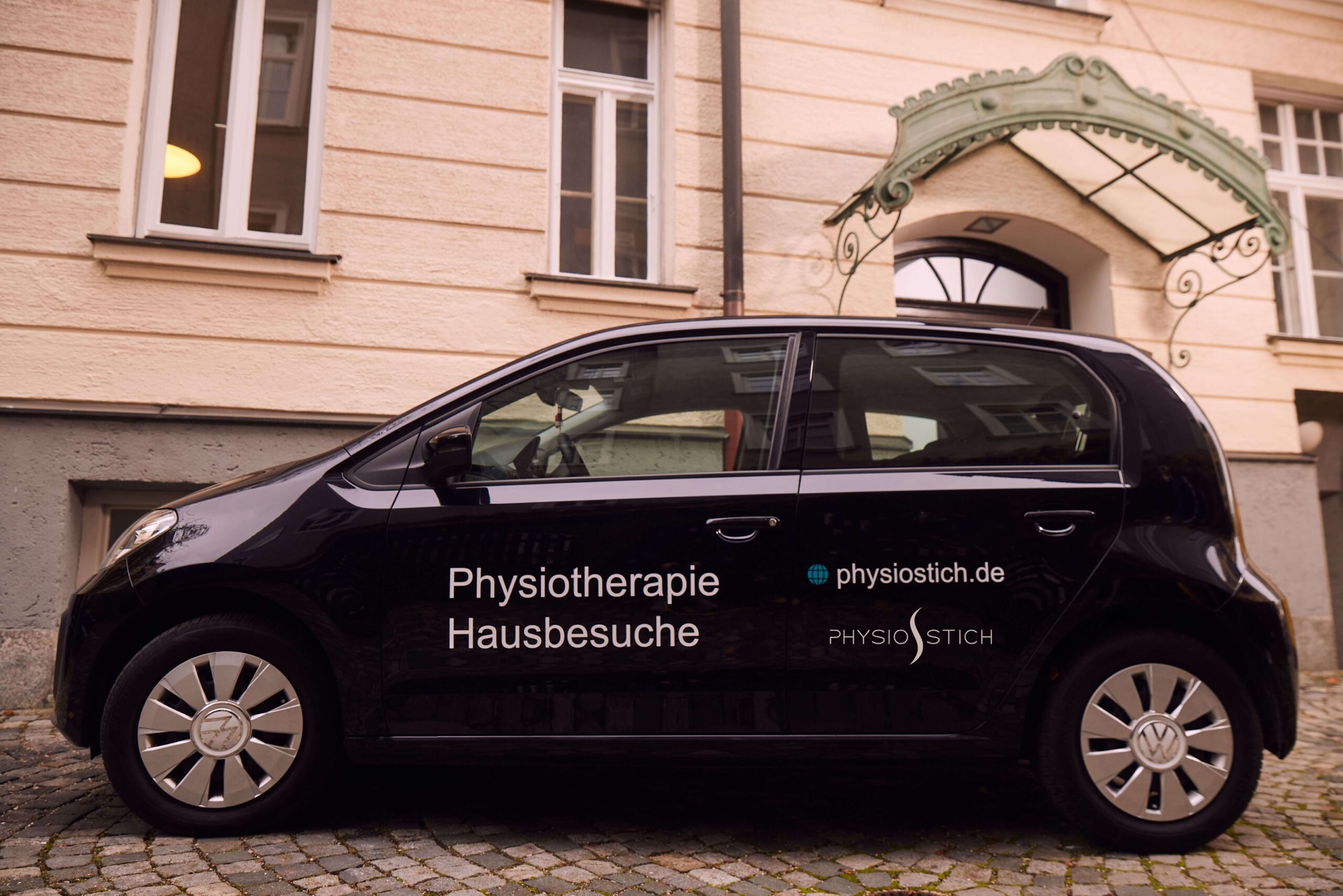 Fahrzeug für mobile Physiotherapie und Krankengymnastik Hausbesuche. Das Firmenauto der Physiotherapiepraxis ist schwarz und mit Werbung beklebt. Die Praxis bietet Physiotherapie zu Hause beim Patienten an.