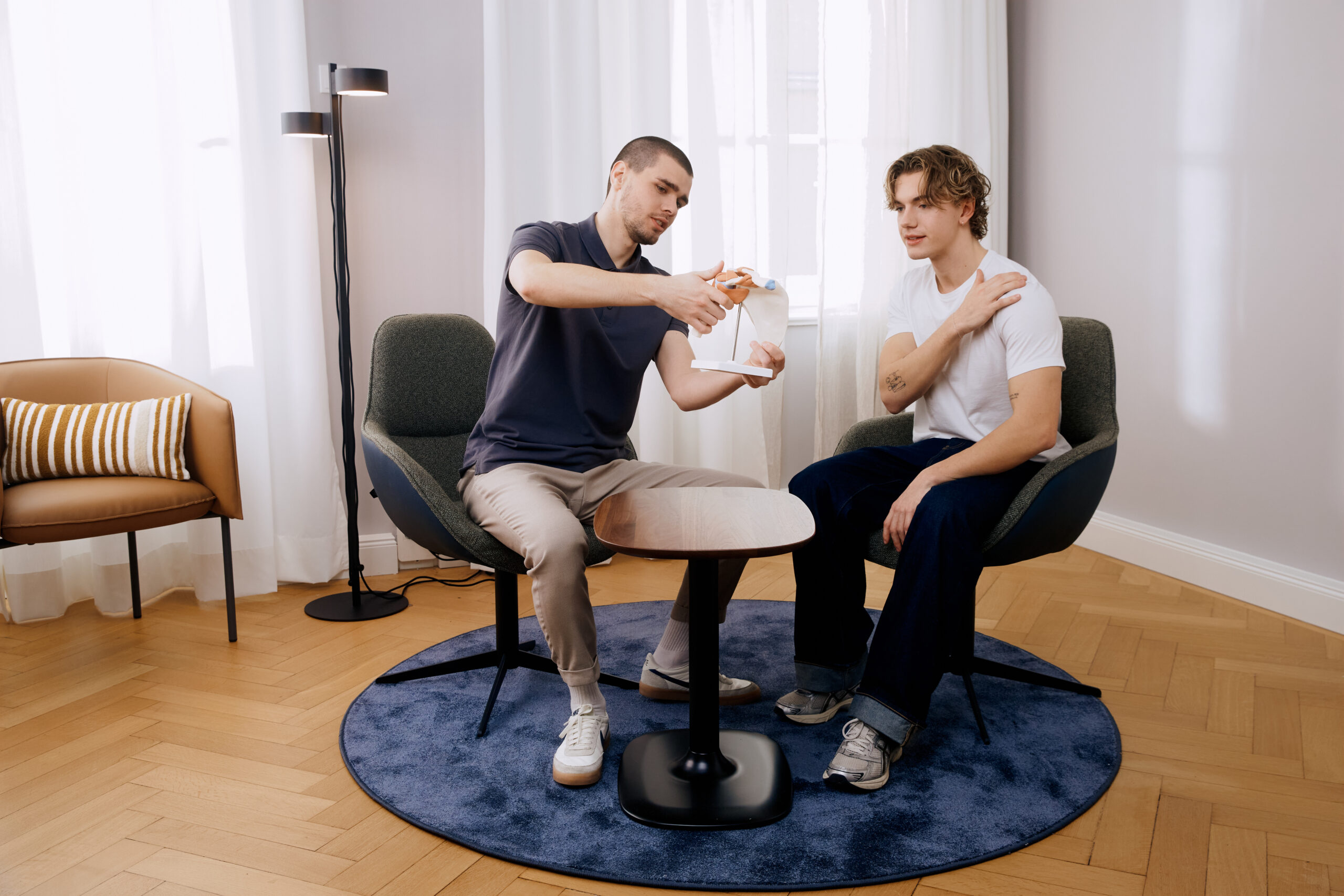 Mann demonstriert Schulterübung mit anatomischem Modell im Beratungsgespräch