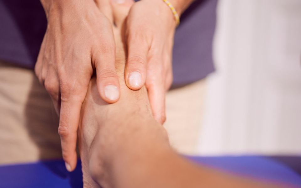 Hände massieren Fuß auf einer blauen Liege.