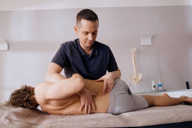 Physiotherapeut massiert Patient auf Liege im Behandlungsraum.