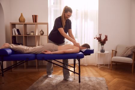 Ein männlicher Patient wird durch eine erfahrene Physiotherapeutin bei einem Physiotherapie Hausbesuch massiert