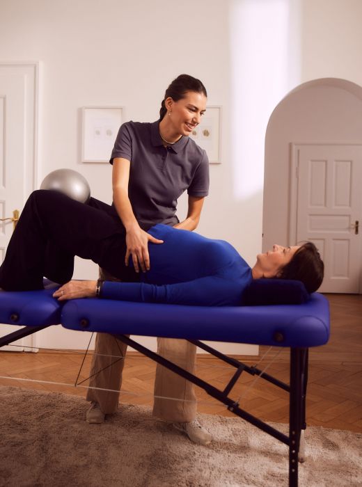 Frau auf Liege, Physiotherapeutin hilft, in Behandlungsraum.