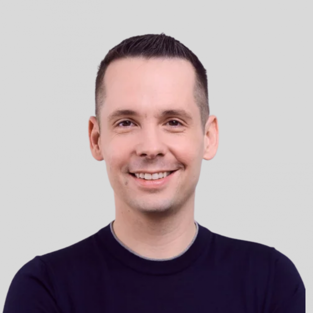 Ein lächelnder Mann im Poloshirt vor neutralem Hintergrund.