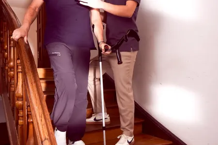 Älterer Mann geht Treppe hinunter, begleitet von Physiotherapeut.