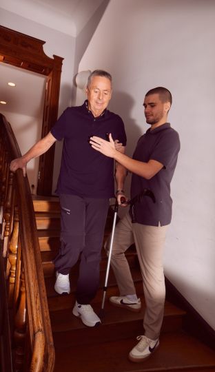 Älterer Mann wird beim Treppensteigen von Pflegekraft unterstützt.