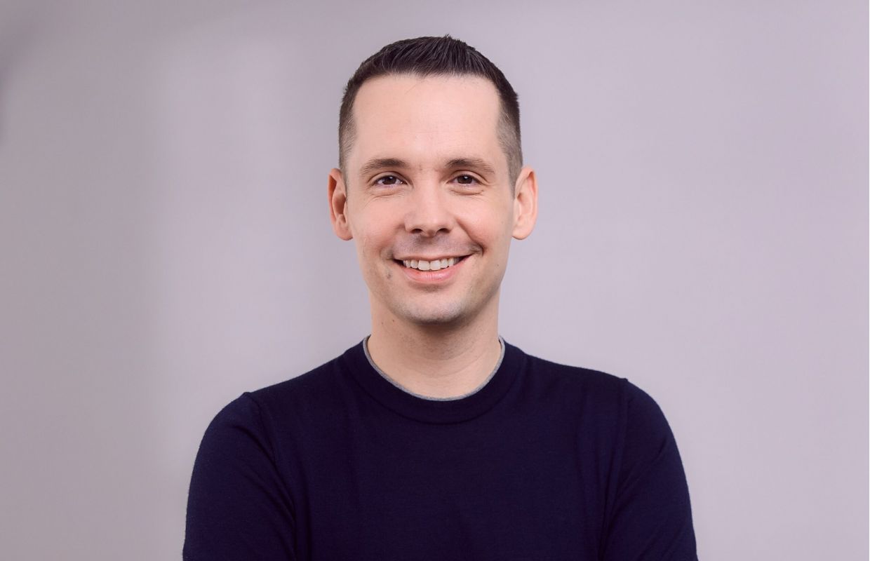 Inhaber und Unternehmer einer privaten Physiotherapiepraxis, welche auf Hausbesuche in Hamburg, Berlin, Frankfurt, Wiesbaden, Mainz, Taunus, München, Bonn, Köln und Düsseldorf spezialisiert ist. Die stationäre Praxis befindet sich in München-Schwabing. Der Chef der Physiotherapiepraxis sitzt auf einer blauen, mobilen Physiotherapiebank bei einem Patienten zu Hause in der Wohnung, trägt eine beige Hose und einen blauen Pullover. Er lächelt in die Kamera.