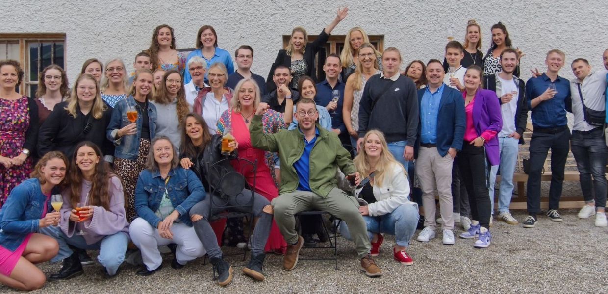 Praxisfest einer Physiotherapiepraxis im Sommer 2024. Alle Physiotherapeuten und Physiotherapeutinnen lächeln in die Kamera und haben gute Laune. Sie stehen vor einem Haus mit Blumenkästen an den Fenstern. Die beiden Praxisinhaber befinden sich ebenso auf dem Foto.