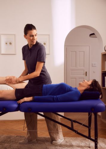 Physiotherapeutin behandelt das Knie einer Patienten bei einem Physiotherapie Hausbesuch. Sie hat eine professionelle Liege mit dabei.