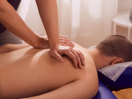 Therapeut massiert Rücken, liegt auf Massagetisch in Therapieumgebung.
