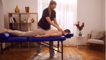 Ein männlicher Patient wird durch eine erfahrene Physiotherapeutin bei einem Physiotherapie Hausbesuch massiert