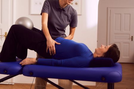 Frau auf Liege, Physiotherapeutin hilft, in Behandlungsraum.