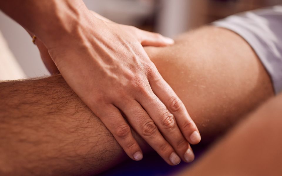 Hand massiert Beinmuskel in therapeutischer Umgebung.