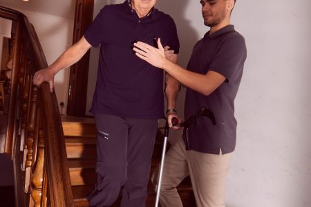 Älterer Mann wird beim Treppensteigen von Pflegekraft unterstützt.