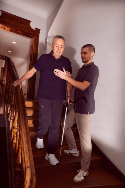 Älterer Mann wird beim Treppensteigen von Pflegekraft unterstützt.