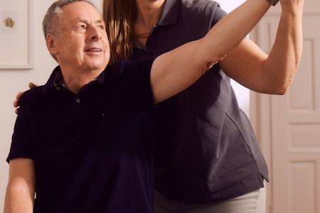 Therapeutin unterstützt älteren Mann bei Armübung im Behandlungsraum.
